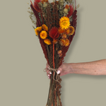 Bouquet titled "Autumn Ember Bouquet" is designed to be a magnificent focal point, perfect for a large vase on a dining table, an entryway, or a mantelpiece. In this photo it is held by a hand against a plain green background.