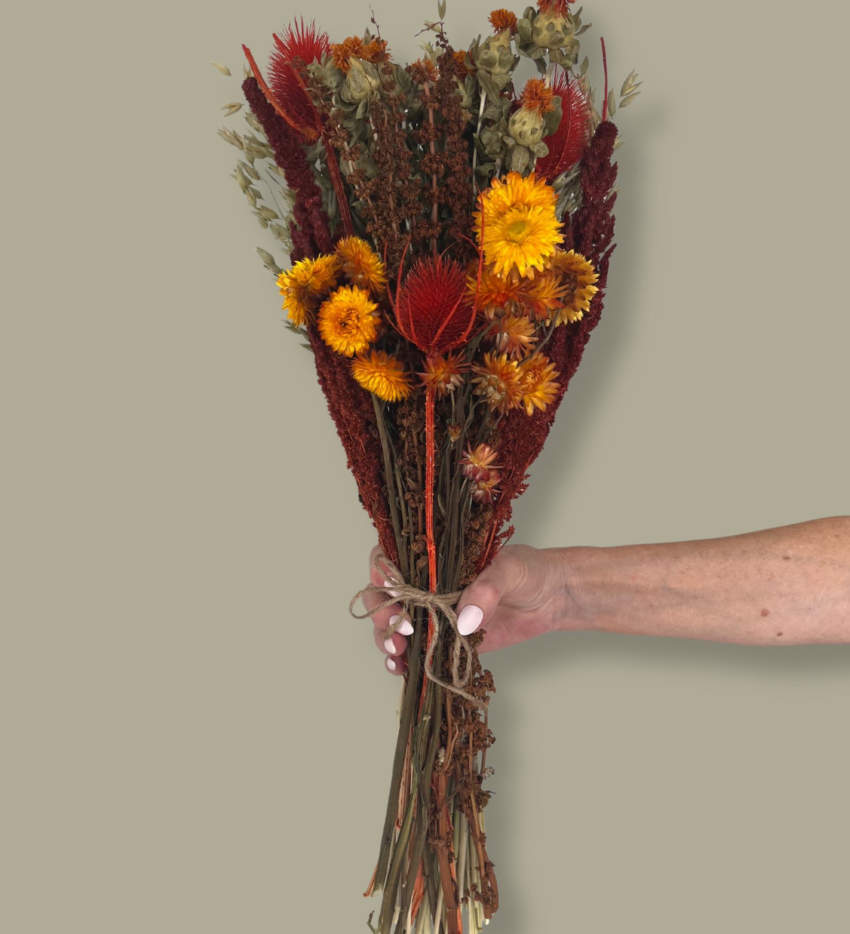 Bouquet titled "Autumn Ember Bouquet" is designed to be a magnificent focal point, perfect for a large vase on a dining table, an entryway, or a mantelpiece. In this photo it is held by a hand against a plain green background.