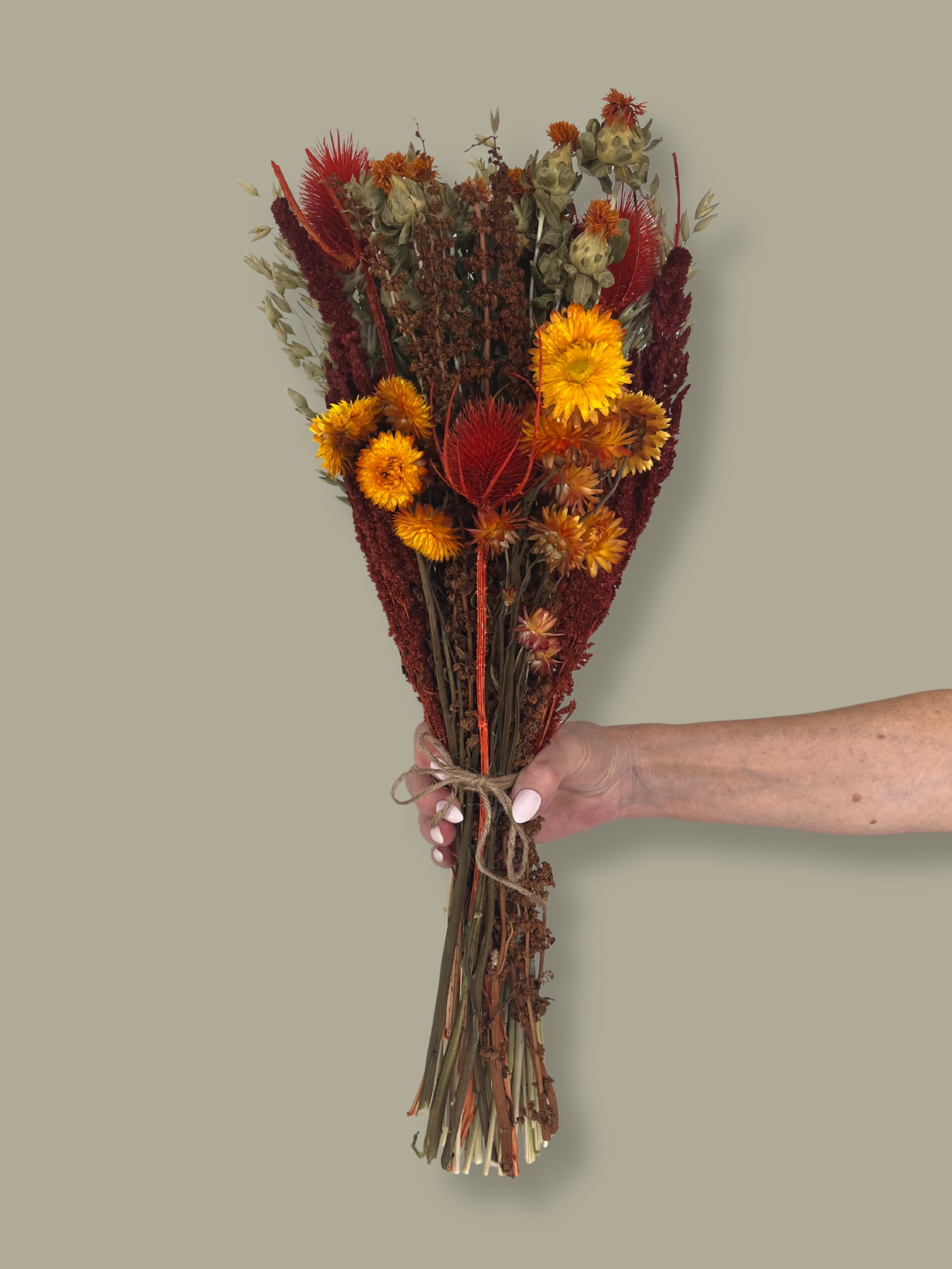 Bouquet titled "Autumn Ember Bouquet" is designed to be a magnificent focal point, perfect for a large vase on a dining table, an entryway, or a mantelpiece. In this photo it is held by a hand against a plain green background.