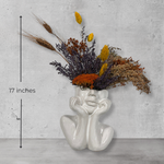 White ceramic vase shaped like a face with dried flowers on a grey concrete background with measurement of 17 inches high