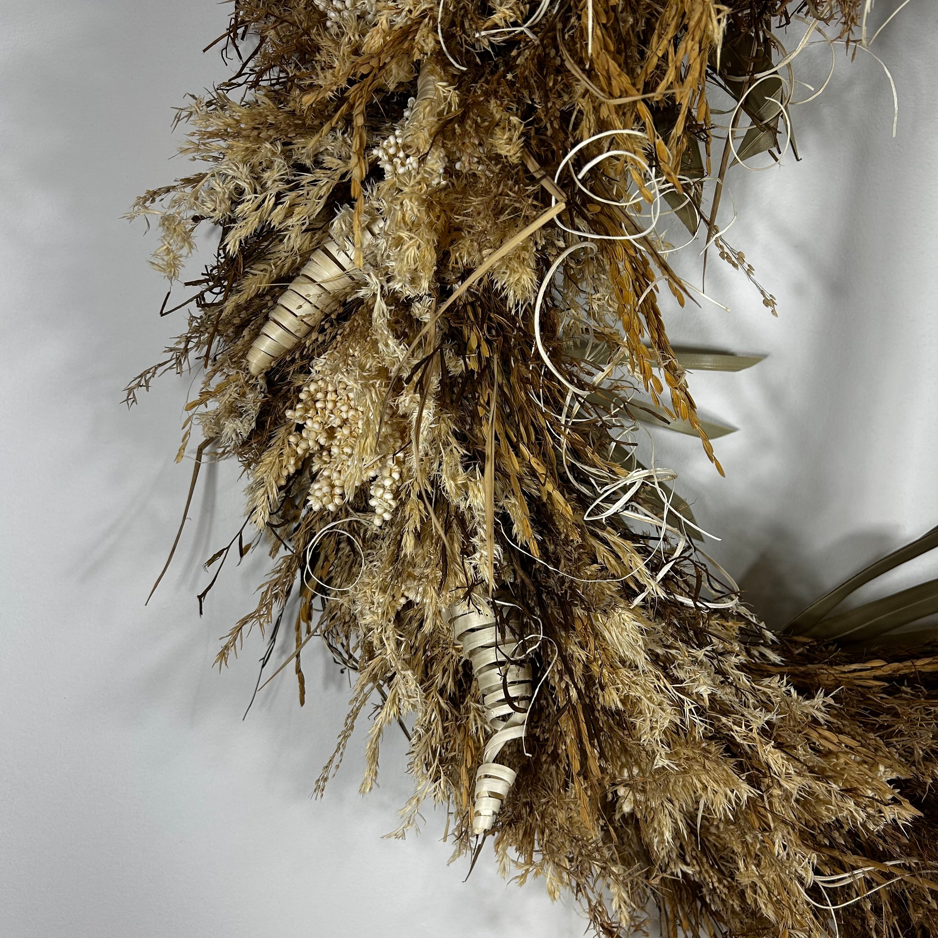 A dried floral arrangement featuring pampas grass, small beige berries, striped dried stems, and curled white wire accents, photographed against a plain light gray background.