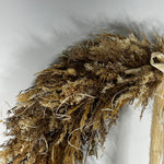 A dried floral arrangement featuring pampas grass, small beige berries, and a light tan ribbon, photographed against a plain light gray background.