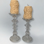 Two decorative candles embossed with sunflowers on glass candlesticks on a light gray background