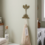 Decorative gold coloured wall hook with bee and 3 leaves, with a laundry bag and bottle in a laundry room.