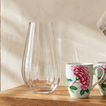 Two floral mugs and a clear vase on a wooden shelf in a kitchen setting.