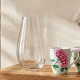 Two floral mugs and a clear vase on a wooden shelf in a kitchen setting.
