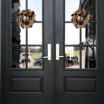 Black double doors with glass panels featuring wreaths, reflecting a residential area.