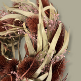 Close-up of the left side of a meticulously crafted 10-inch accent wreath with it's lush burgundy red teasels providing a striking focal point against the delicate, ethereal sprays of Bupleurum in a soft pink and natural willow eucalyptus adds a graceful touch of olive green.