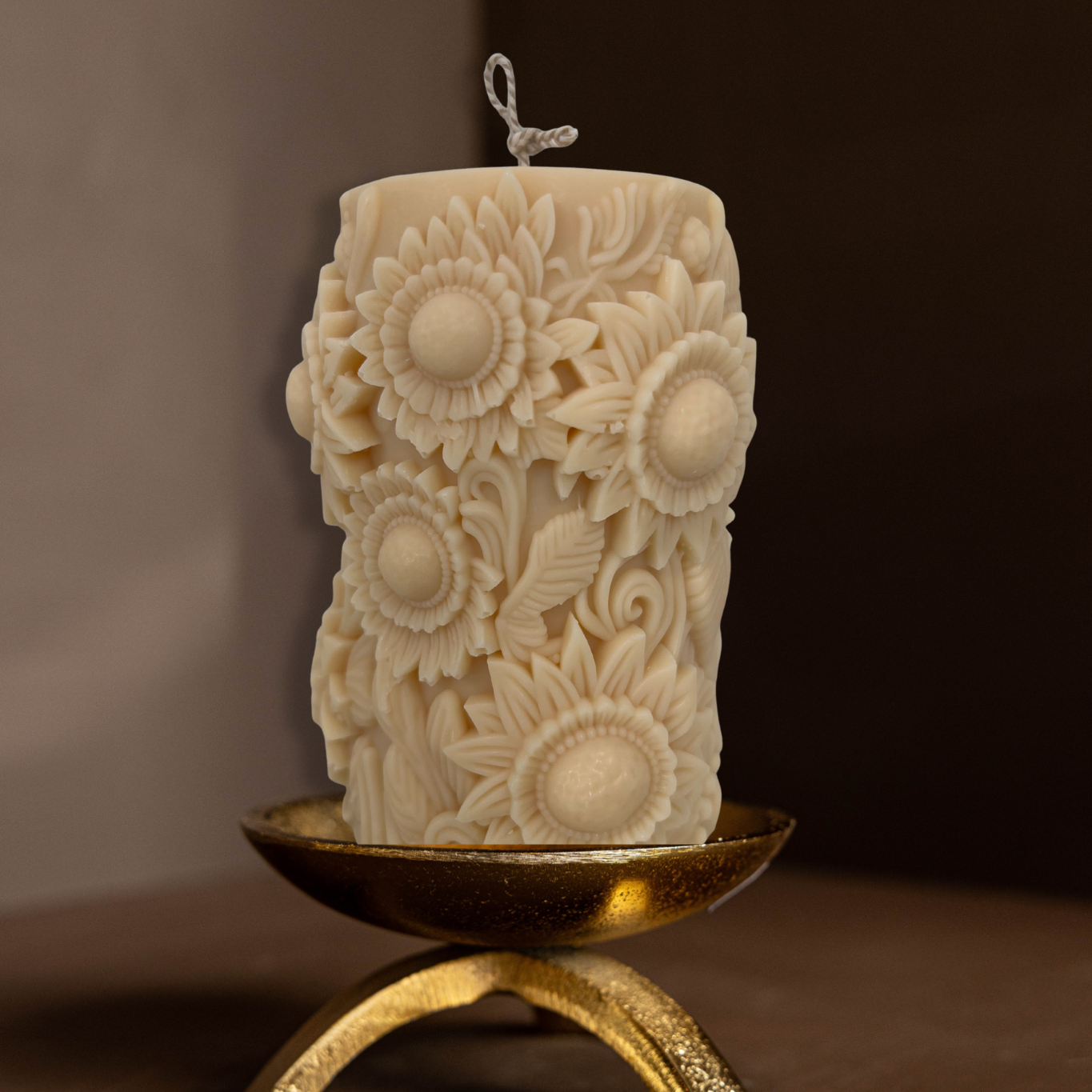 Decorative candle with sunflower patterns on a brass tripod pillar candle holder against a brown background