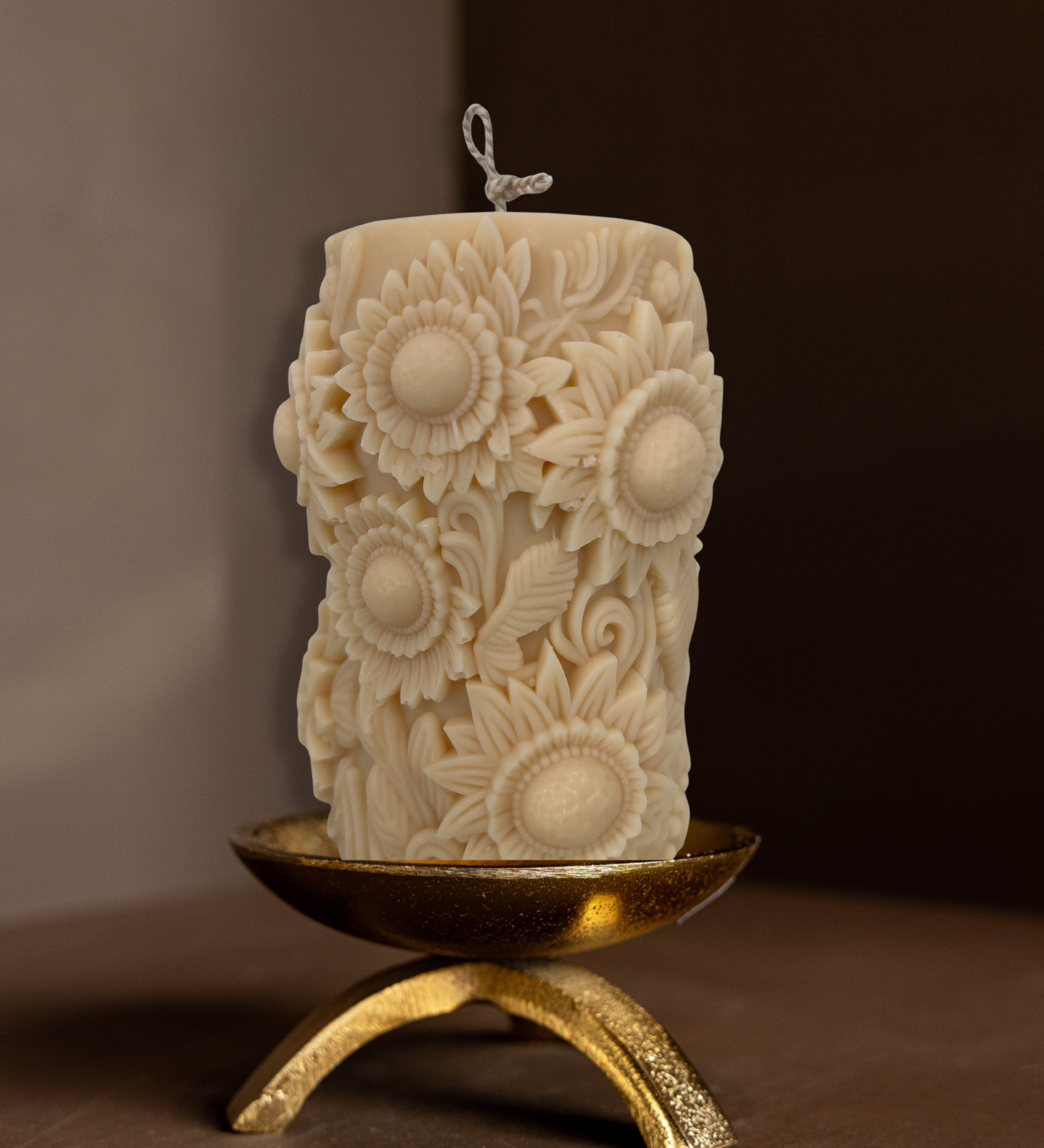 Decorative candle with sunflower patterns on a brass tripod pillar candle holder against a brown background