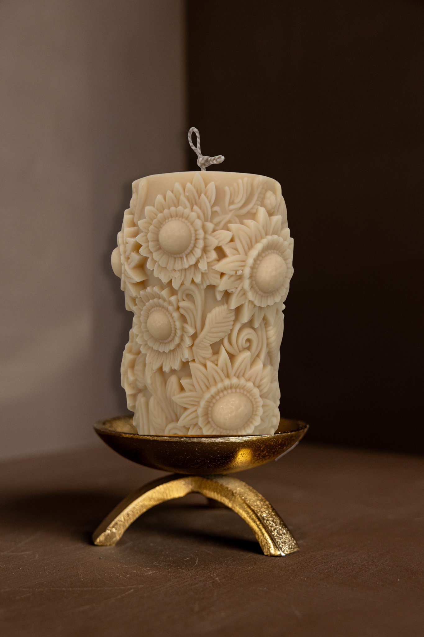 Decorative candle with sunflower patterns on a brass tripod pillar candle holder against a brown background