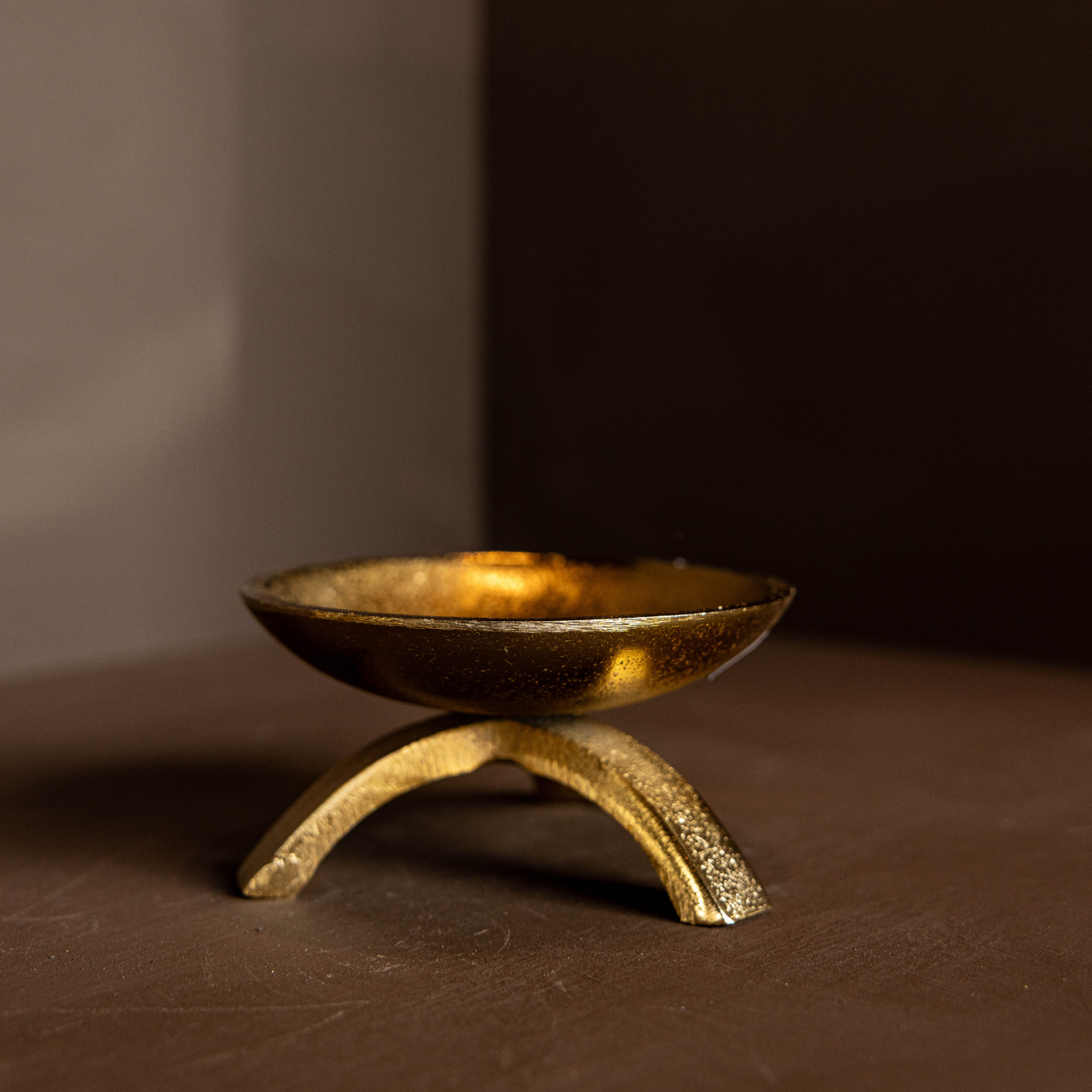 Brass tripod pillar candle holder on a brown surface with a dark background