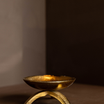 Brass tripod pillar candle holder on a brown surface with a dark background
