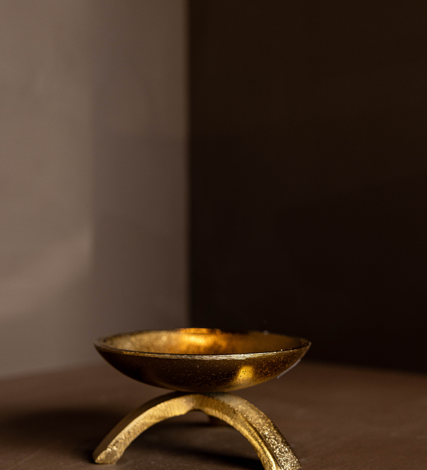 Brass tripod pillar candle holder on a brown surface with a dark background