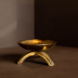 Brass tripod pillar candle holder on a brown surface with a dark background