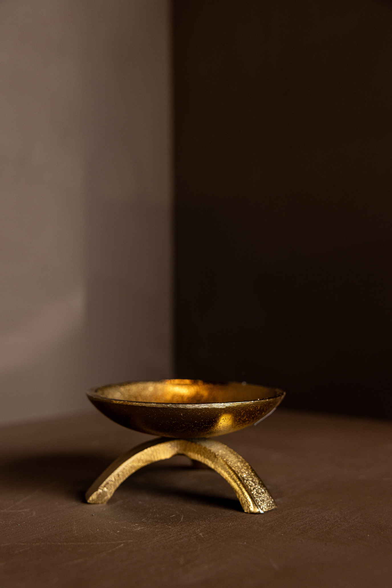 Brass tripod pillar candle holder on a brown surface with a dark background