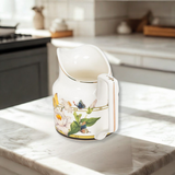Decorative white creamer with floral and butterfly design on a kitchen counter.