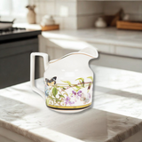 Decorative white creamer with floral and butterfly design on a kitchen counter.