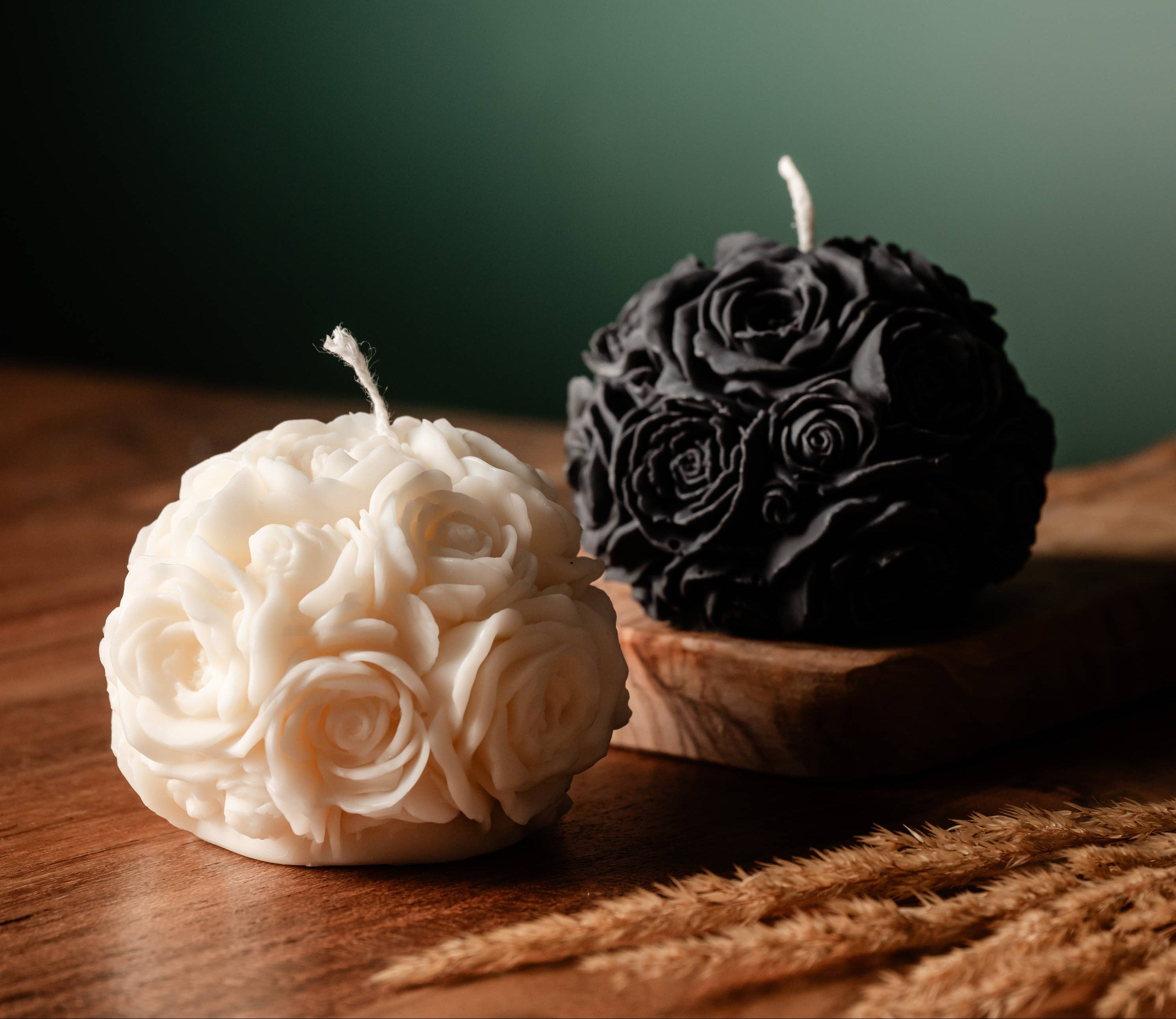 Two spherical candles, one white and one black, with rose patterns on a wooden surface.
