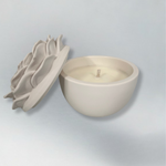 Decorative candle in container with floral designed lid. Lid has been removed.