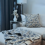Living room with a soft grey sofa, blue and ivory floral-patterned cushions and matching throw, and a small table with a dried flower arrangement in a vase. 1