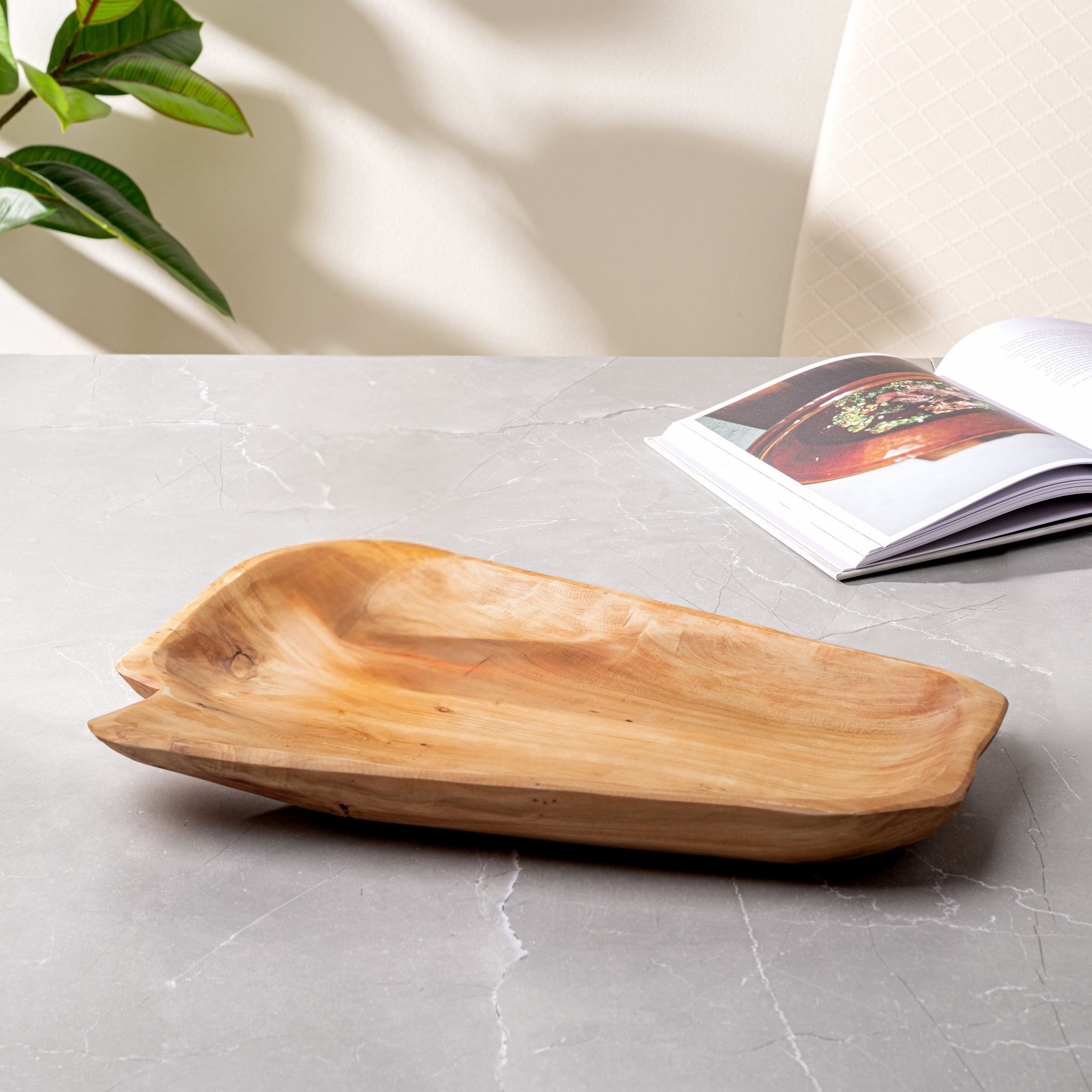 Wooden tray on a gray surface with a magazine and plant in the background