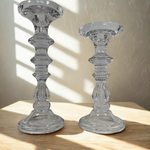Two clear glass candle holders on a wooden surface with a neutral background