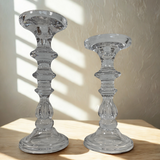 Two clear glass candle holders on a wooden surface with a neutral background