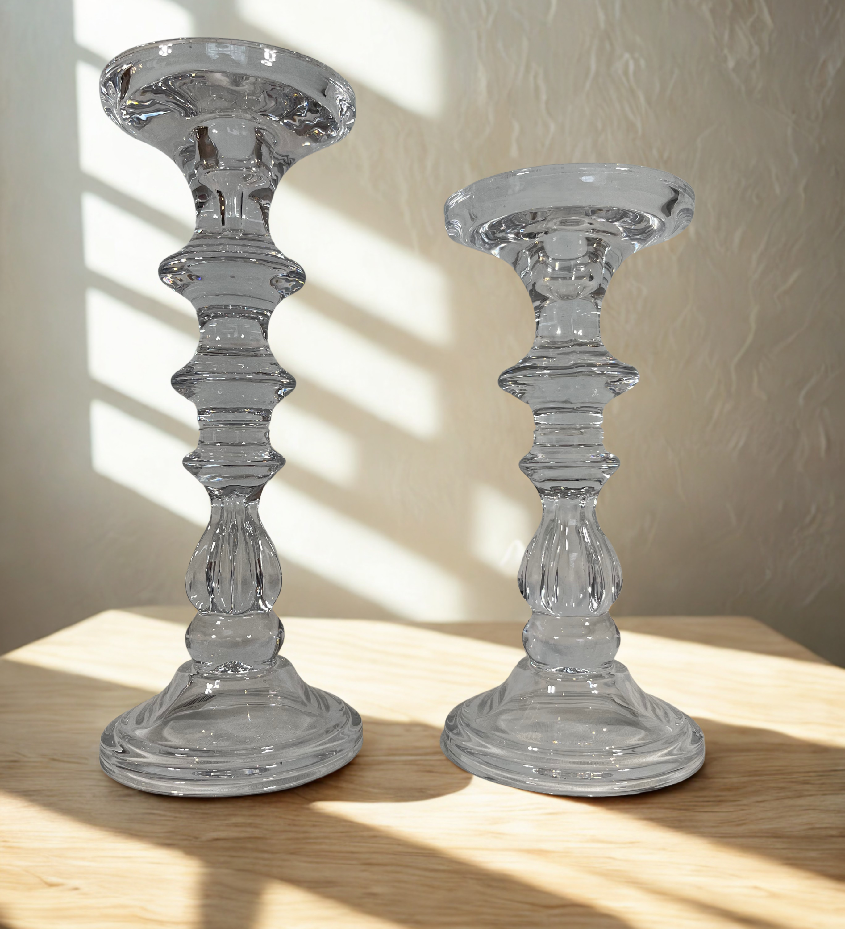 Two clear glass candle holders on a wooden surface with a neutral background