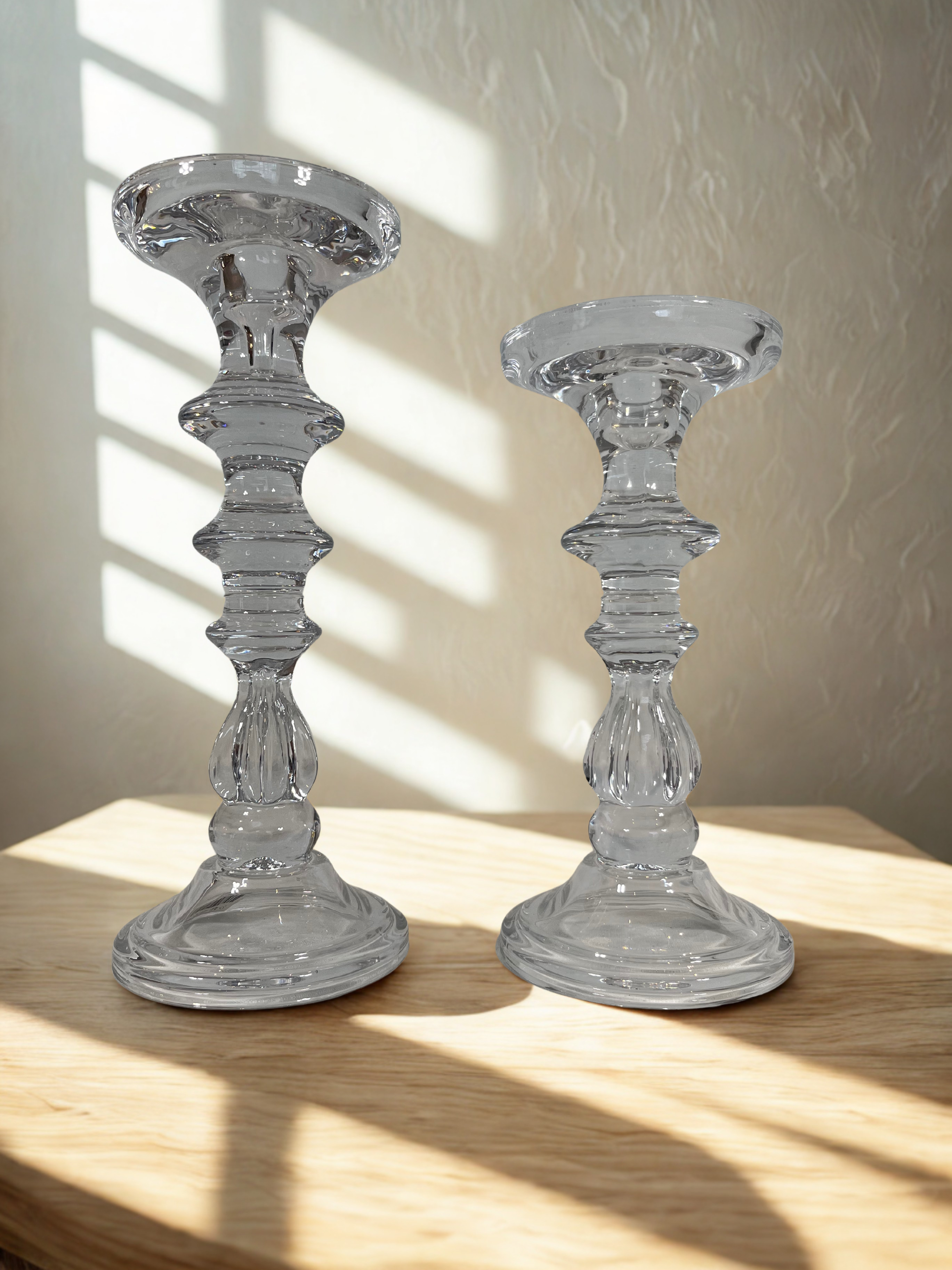 Two clear glass candle holders on a wooden surface with a neutral background