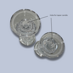 Two glass candle holders with a labeled hole for a taper candle on a light gray background