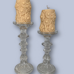 Two ornate glass candlesticks with textured candles on a light blue background