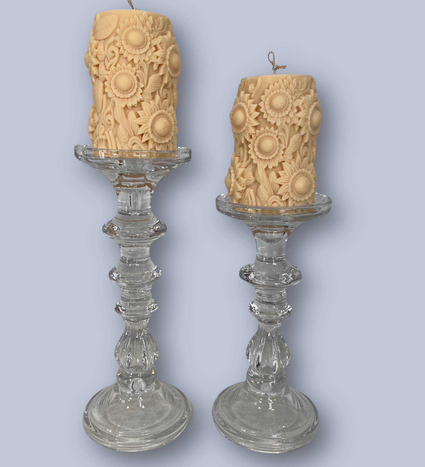 Two ornate glass candlesticks with textured candles on a light blue background