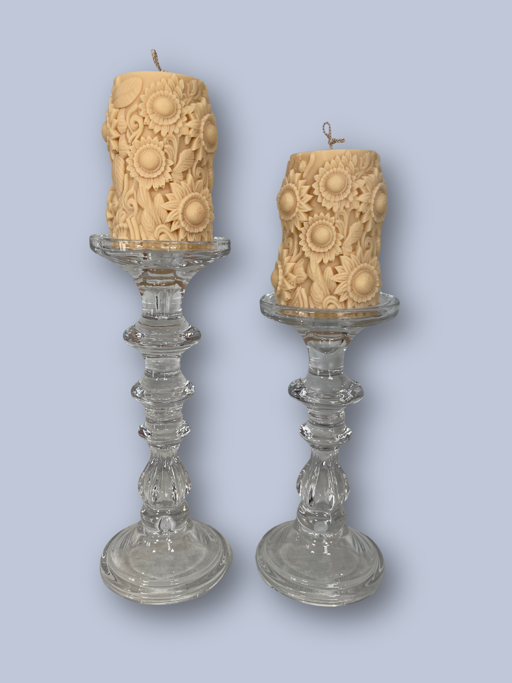 Two ornate glass candlesticks with textured candles on a light blue background