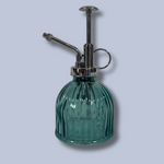 Green glass spray bottle with metal nozzle on a light gray background