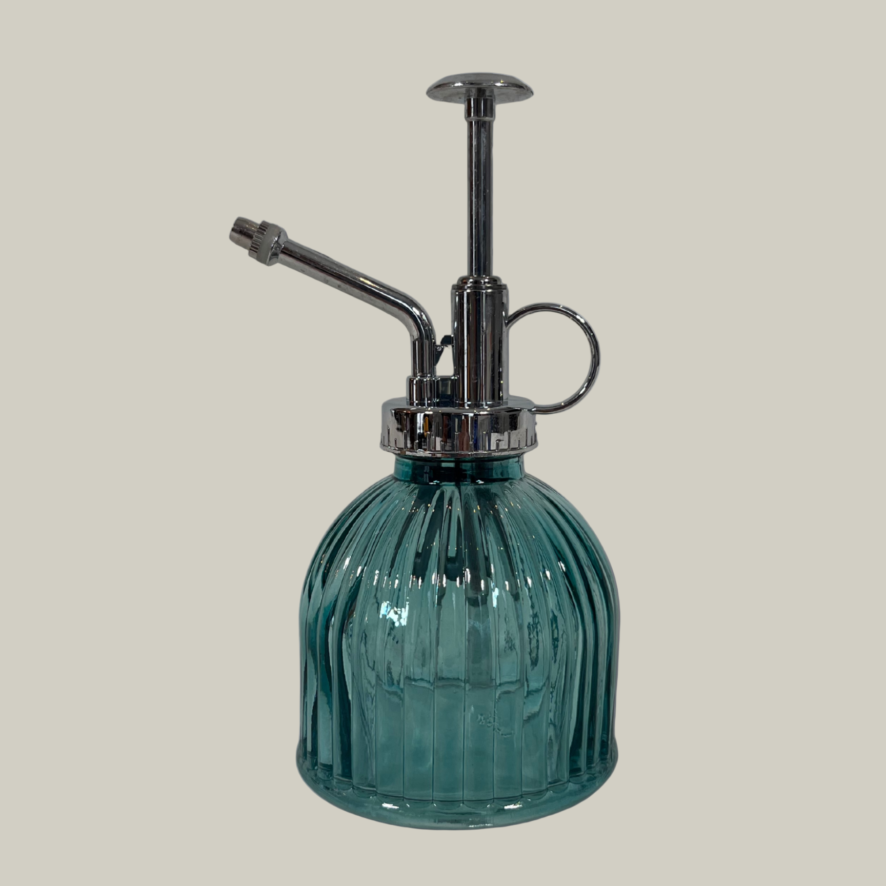 Green glass spray bottle with metal nozzle on a light gray background