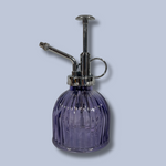 Purple glass spray bottle with silver nozzle on a light gray background