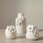 Three white ceramic vases with crackle glaze and floral appliqués on a neutral background
