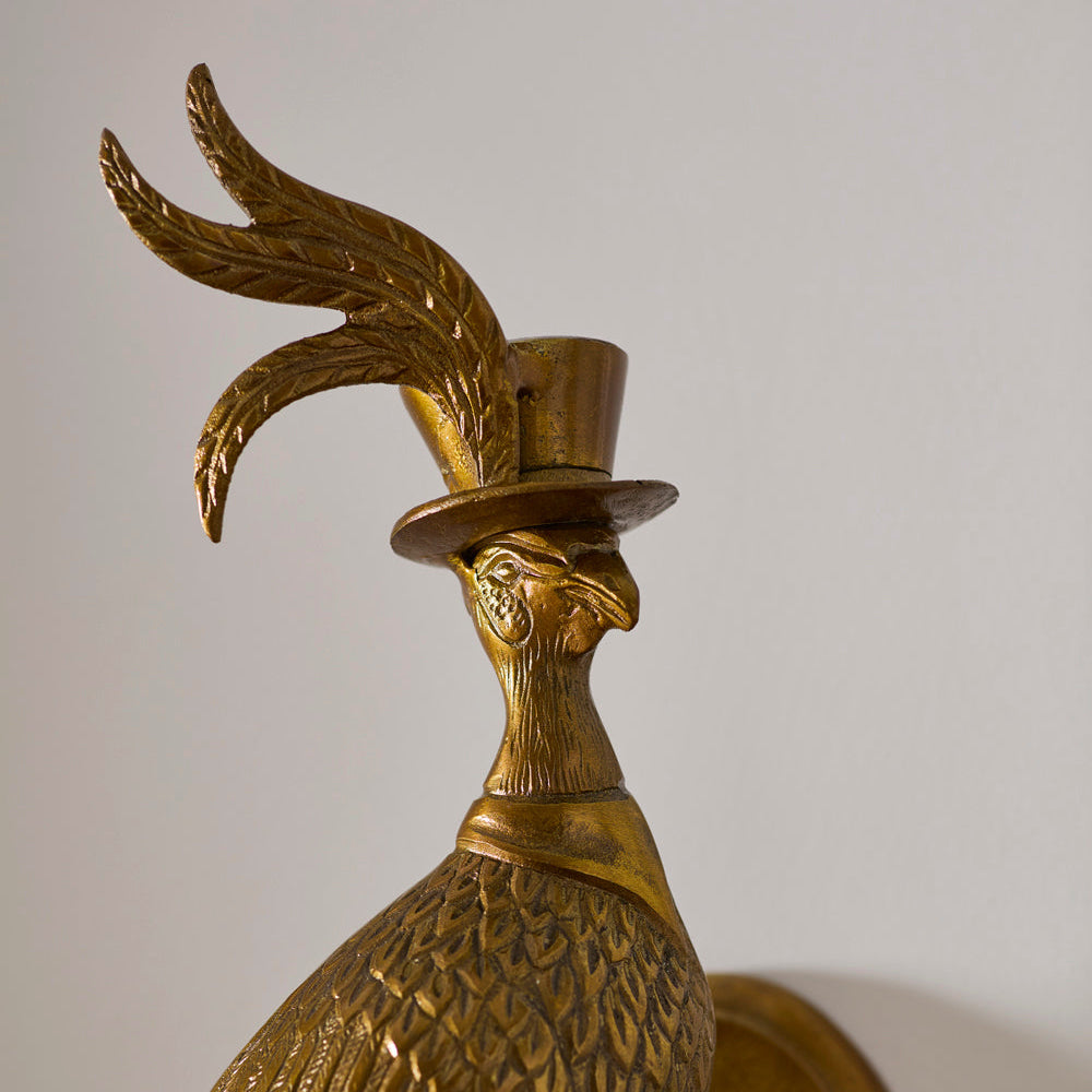 Bronze peacock sculpture wearing a top hat on a plain background
