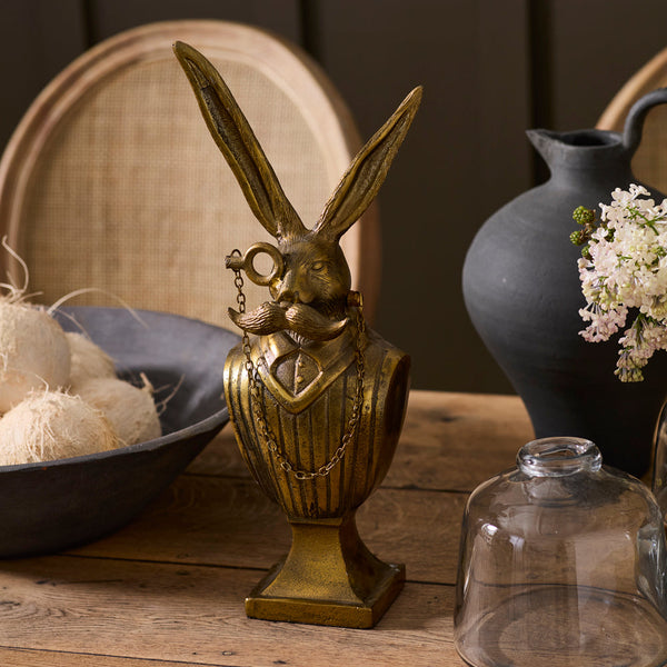 Decorative brass rabbit bust on a wooden surface with a dark background