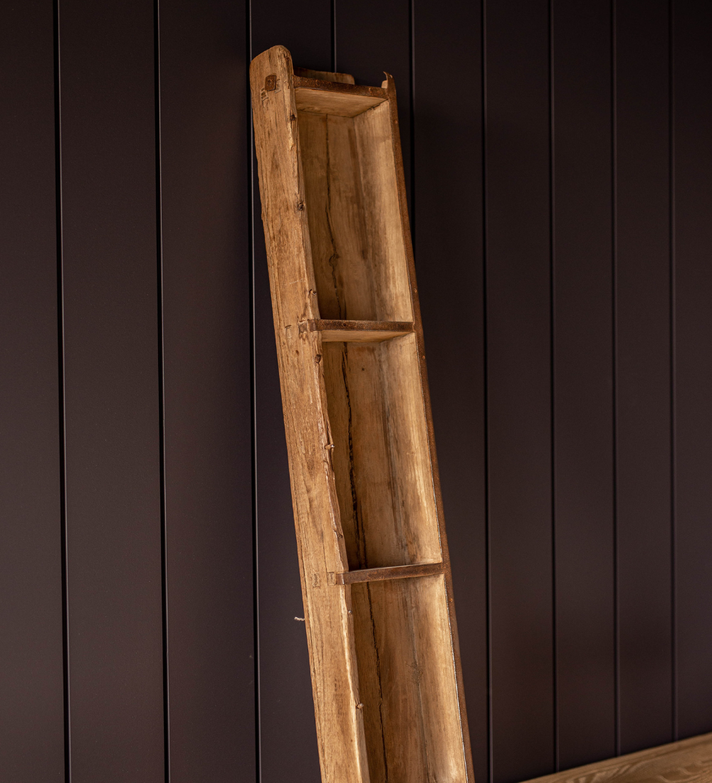 Side view of a tall vintage wooden brick mold standing on it's end against a dark panelled wall