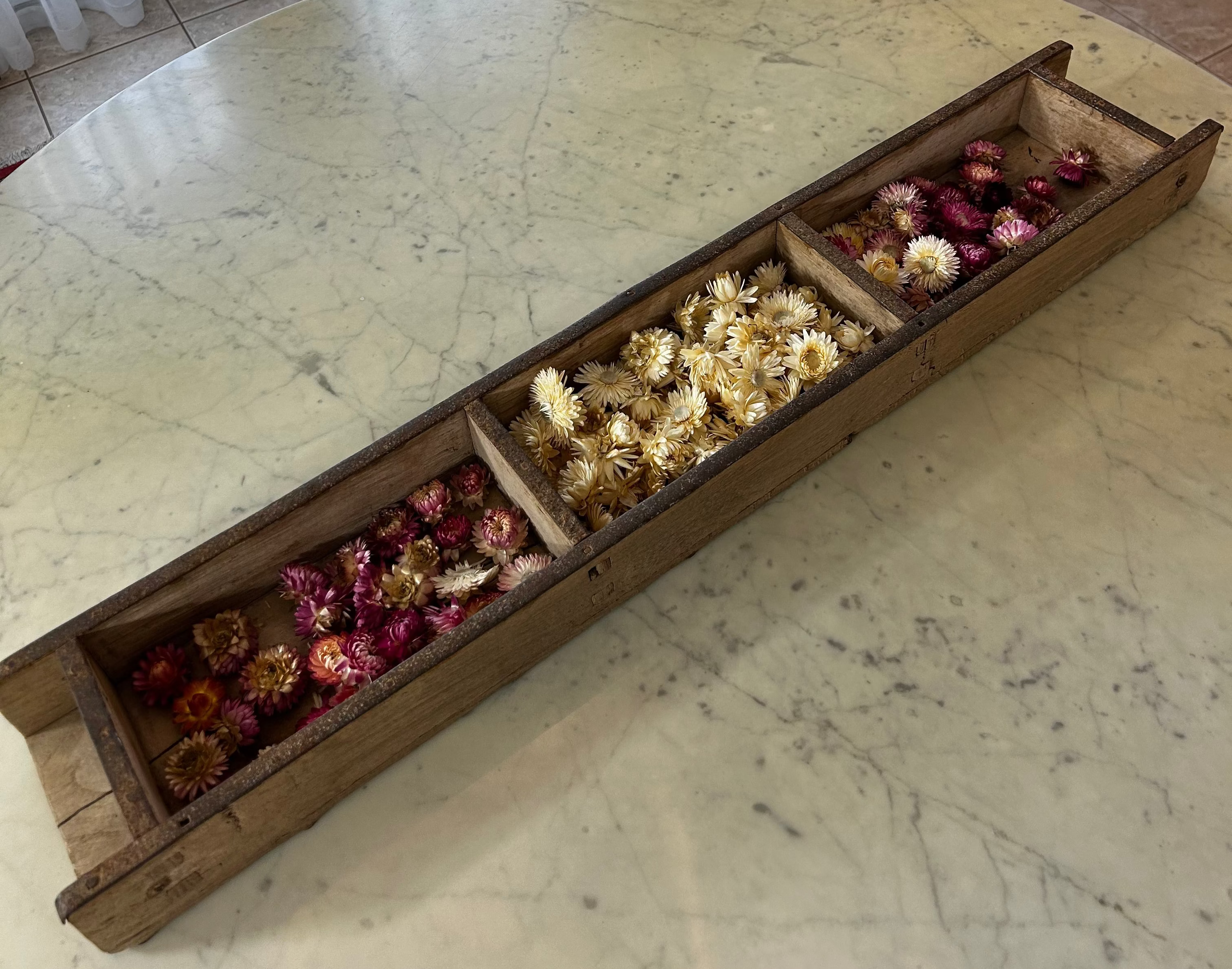 Over view of a tall vintage wooden brick mold filled with dried helichrysums sitting on a marble table
