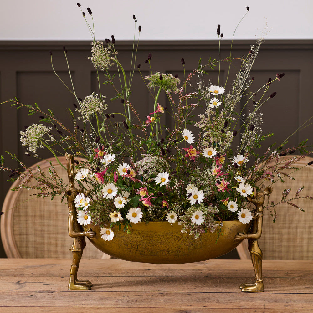 Decorative floral arrangement in a brass bowl on a wooden table with a neutral background