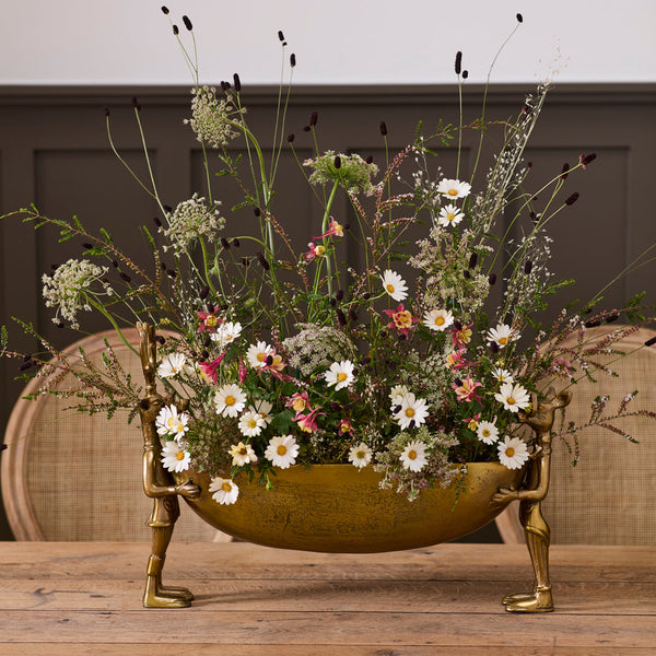 Decorative floral arrangement in a brass bowl on a wooden table with a neutral background
