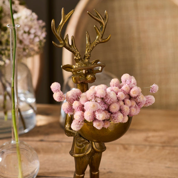 Bronze figurine with antlers holding pink flowers on a wooden surface
