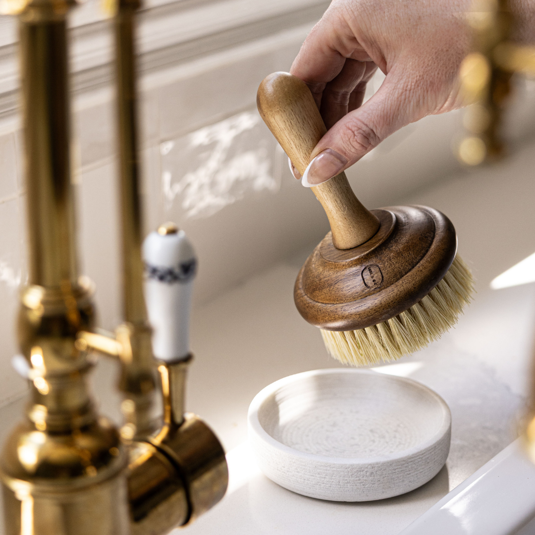 Hand using a wooden brush over a soap dish on a bathroom sink.