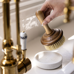 Hand using a wooden brush over a soap dish on a bathroom sink.