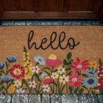 Doormat with floral design and 'hello' text on a stone floor.