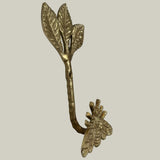 Decorative brass wall hook with leaves and a bee on a beige background