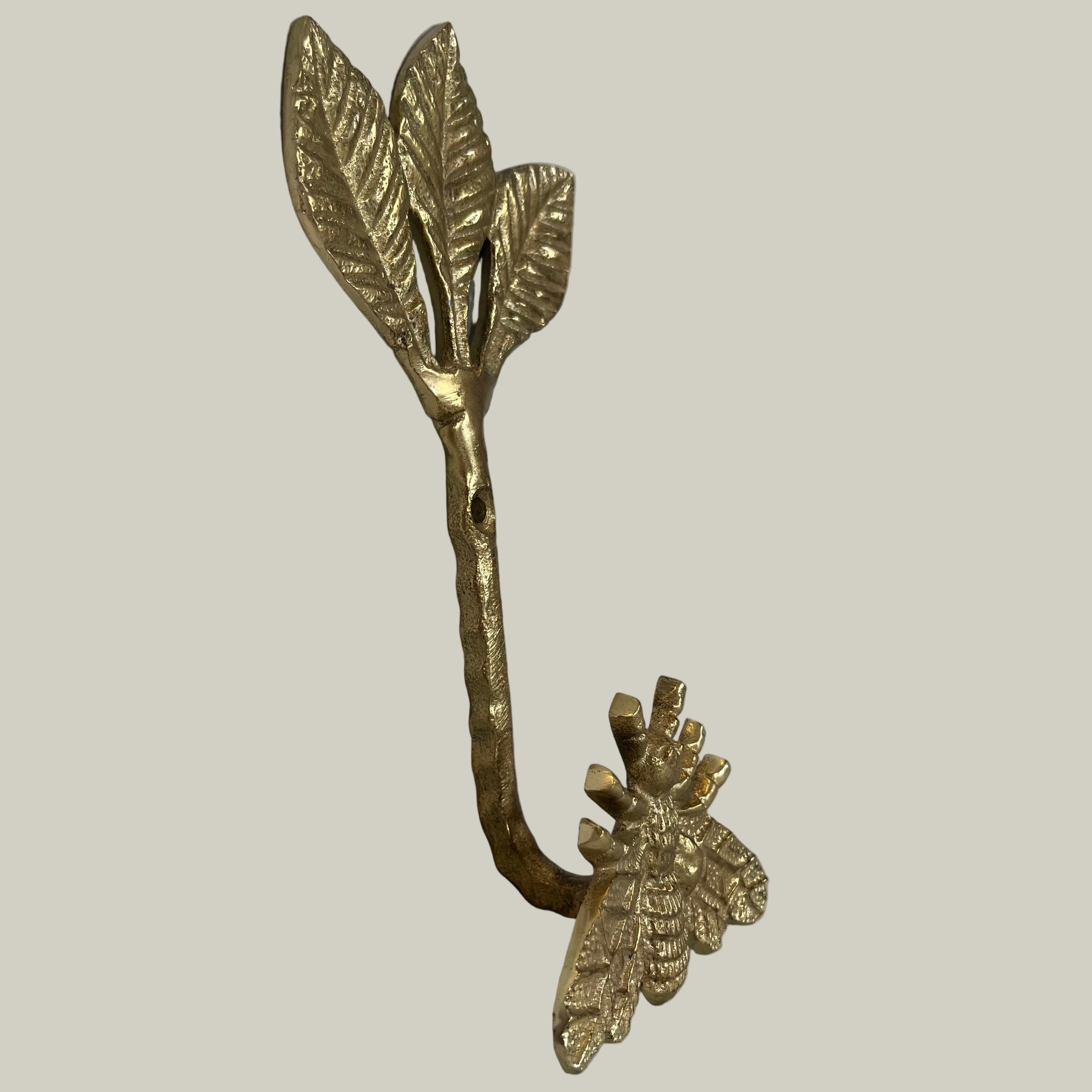 Decorative brass wall hook with leaves and a bee on a beige background